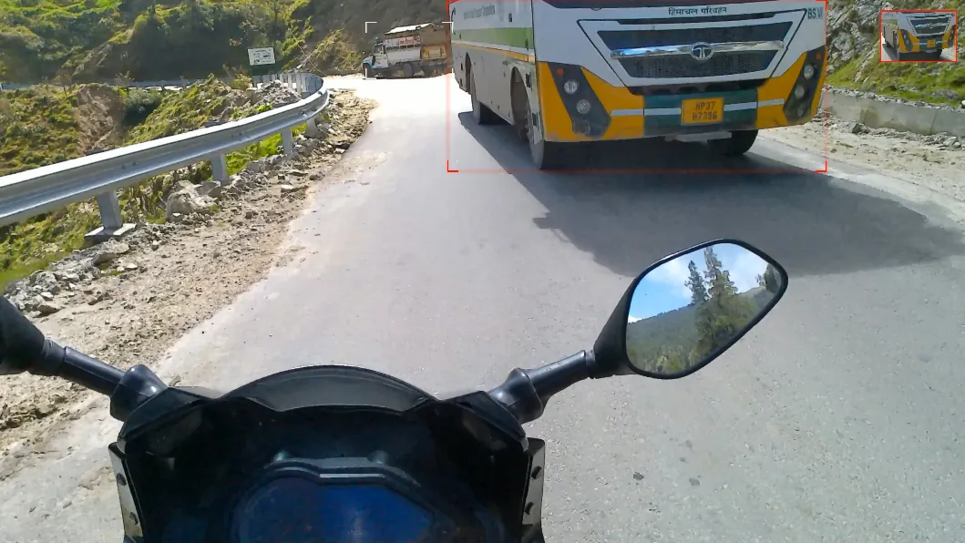 A yellow and green bus coming round a bend on a mountain road, outlined in red corner brackets.
